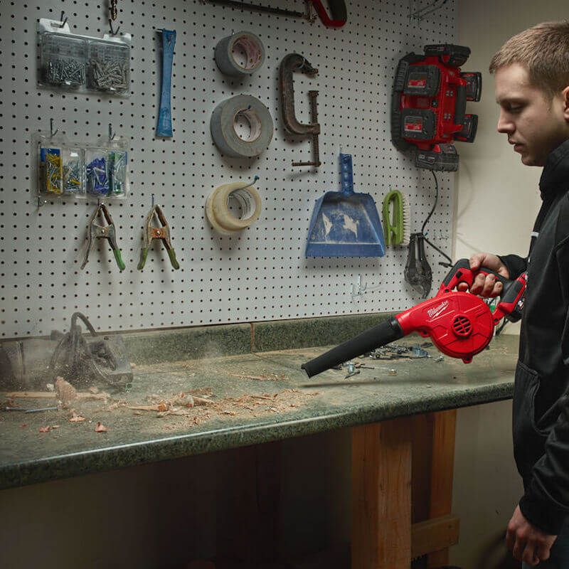 Action shot of the Milwaukee M18 Compact Blower in use, effortlessly cleaning a tight space with its removable nozzle, nozzle extension, variable speed control, and inflator/deflator attachment. Action shot of the Milwaukee M18 Compact Blower in use, effortlessly cleaning a tight space with its removable nozzle, nozzle extension, variable speed control, and inflator/deflator attachment.